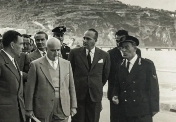 Angelo Rizzoli, con abito scuro, cammina con altri uomini a Ischia, sullo sfondo una collina terrazzata.
