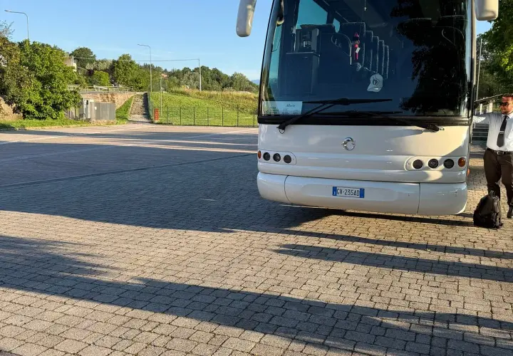 Un bus bianco attende su un parcheggio lastricato, pronto a percorrere le strade di Ischia. Un autista in divisa controlla il bagaglio.