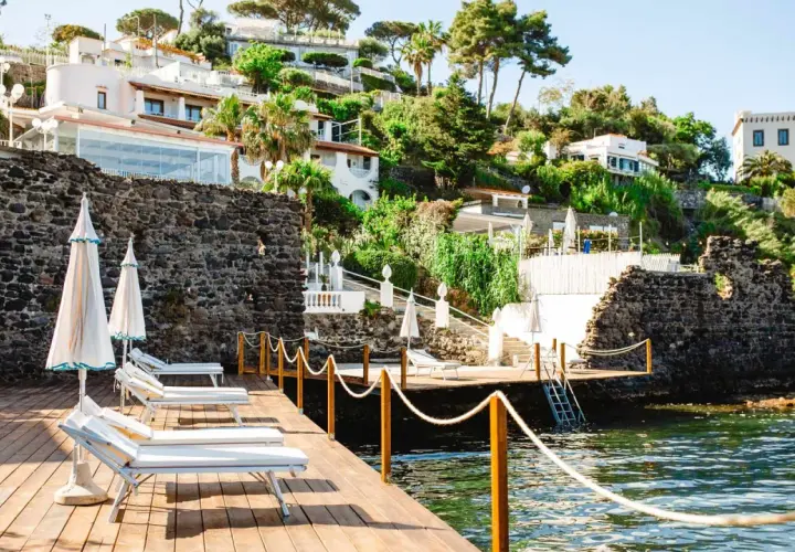 Terrazza in legno con lettini e ombrelloni, vista sul mare e sulle ville del **hotel i delfini Ischia** immerse nel verde.
