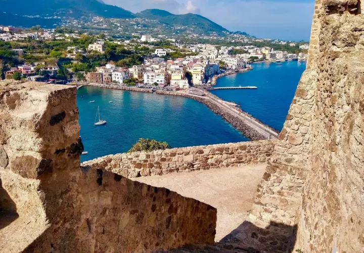 Vista panoramica del porto di Ischia, con i traghetti in attesa e le case colorate che si affacciano sul mare blu.