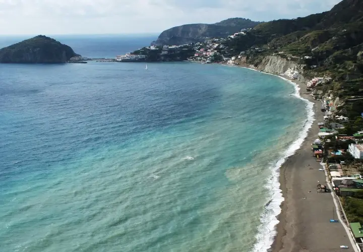 Vista aerea della spiaggia dei pescatori a Ischia, con case colorate aggrappate alla costa e un mare turchese.