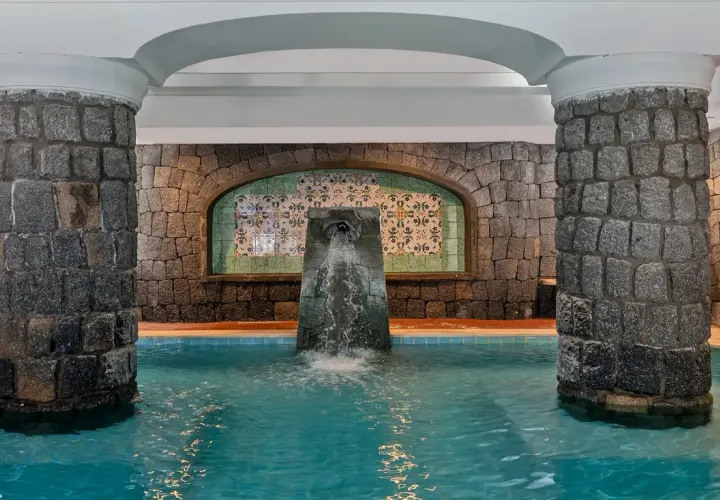 Piscina interna con fontana a cascata, colonne in pietra e piastrelle decorative. Un angolo di relax alle terme di Lacco Ameno.