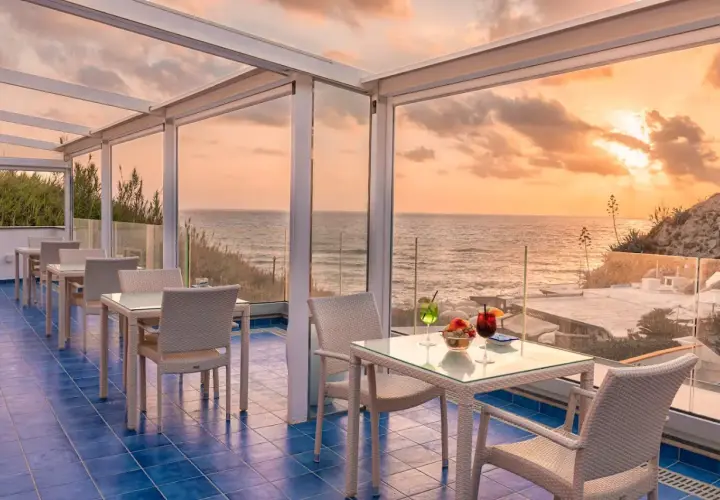 Terrazza con vista mare al tramonto, ideale per chi cerca dove alloggiare a Ischia senza macchina. Tavoli apparecchiati per aperitivo.