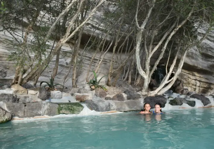 Due bambine si godono un bagno rilassante in una piscina naturale, circondata da rocce e vegetazione, un luogo perfetto per terme gratuite.