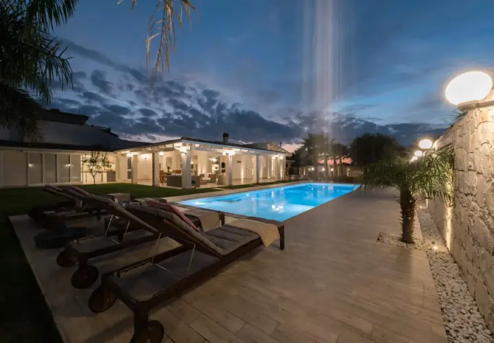 Piscina illuminata e lettini prendisole al tramonto, con cascata d'acqua. Un'oasi di relax al **hotel le palme Ischia**.