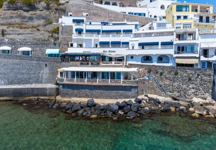 Hotel Celestino Ischia, con la sua architettura bianca e blu, si affaccia sul mare cristallino, incastonato nella roccia.