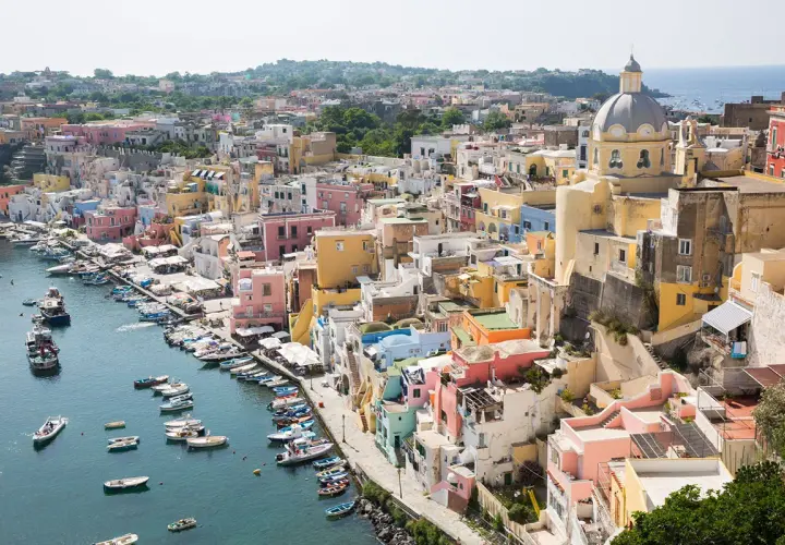 Colorate case a picco sul mare, un porto con barche. La vista ricorda la vicinanza tra Ischia e Capri, un sogno di vacanza.