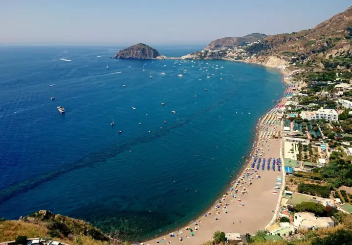 Vista aerea delle spiagge di Ischia, con ombrelloni colorati, mare blu intenso e tante barche all'orizzonte.