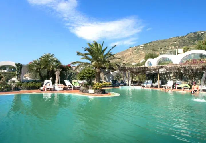 Piscina con palme e lettini, un angolo di paradiso tropicale a Ischia, con persone che si rilassano nell'acqua cristallina.