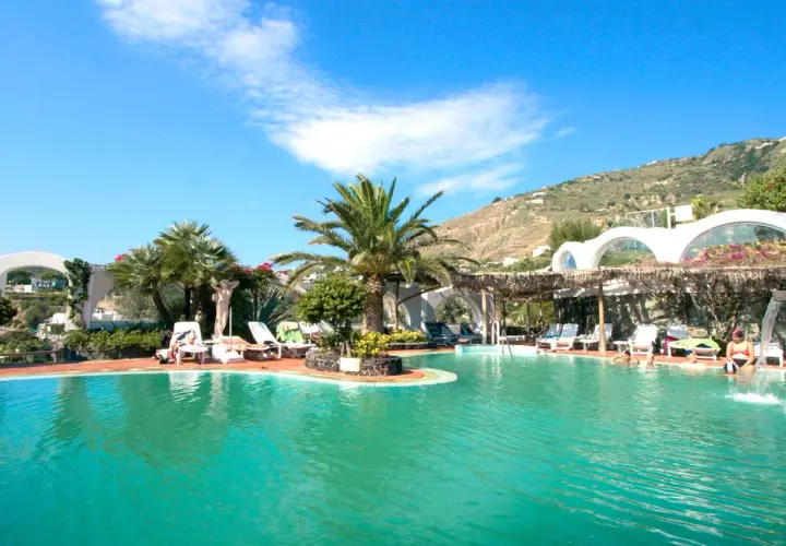 Piscina con lettini e palme, un'oasi di relax alle terme Sant'Angelo Ischia, con vista sulla collina verdeggiante.
