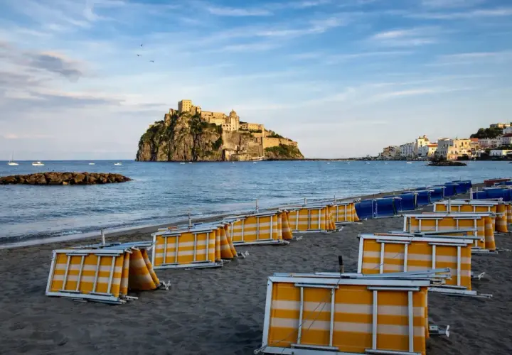 Spiaggia della Mandra a Ischia, con lettini piegati e il Castello Aragonese sullo sfondo.