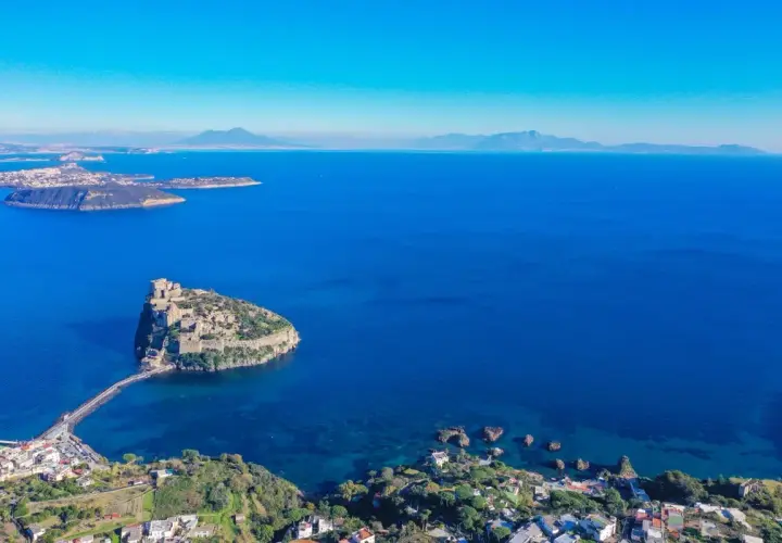 Aerial view of Castello Aragonese on a rocky island connected by a causeway to the coast of Ischia, Italy.