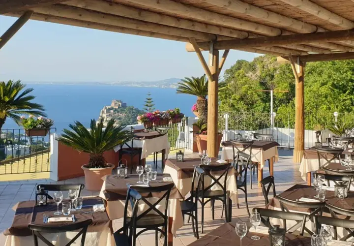 Terrazza con tavoli apparecchiati e vista mare a Ischia. Un vero nascondiglio dell'amore, perfetto per una cena romantica.
