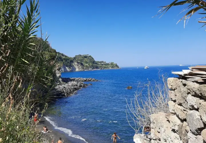 Spiaggia nera con gente che si gode il sole, scogli e il blu intenso del mare degli inglesi.