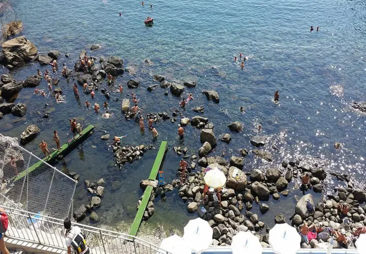 Persone si godono il sole e l'acqua cristallina nelle piscine naturali di Ischia, tra scogli e fondali trasparenti.