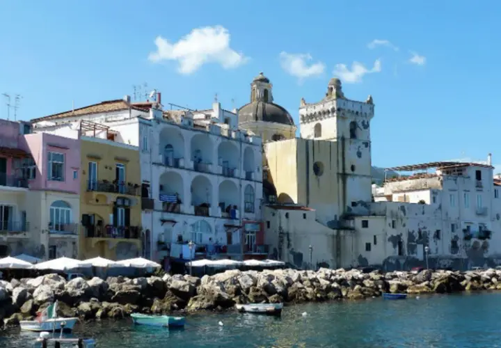 Colorate case affacciate sul mare, un porto con barche e rocce. Per sapere come arrivare ad Ischia in treno, si può prendere un treno per Napoli e poi un aliscafo.