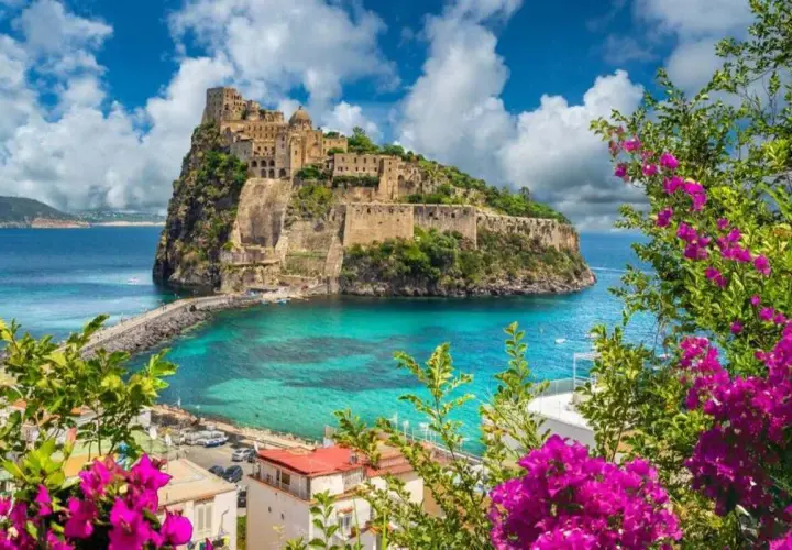 Castello Aragonese su uno scoglio, con mare turchese e fiori viola in primo piano. Una vittoria colonna di bellezza naturale.