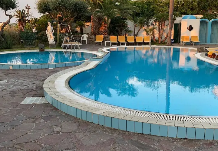 Piscine azzurre e lettini gialli al **hotel Monte Tabor**, un'oasi di relax tra palme e statue.