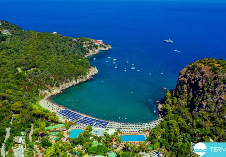 Vista aerea di una baia con spiaggia, mare blu e le piscine Negombo immerse nel verde.