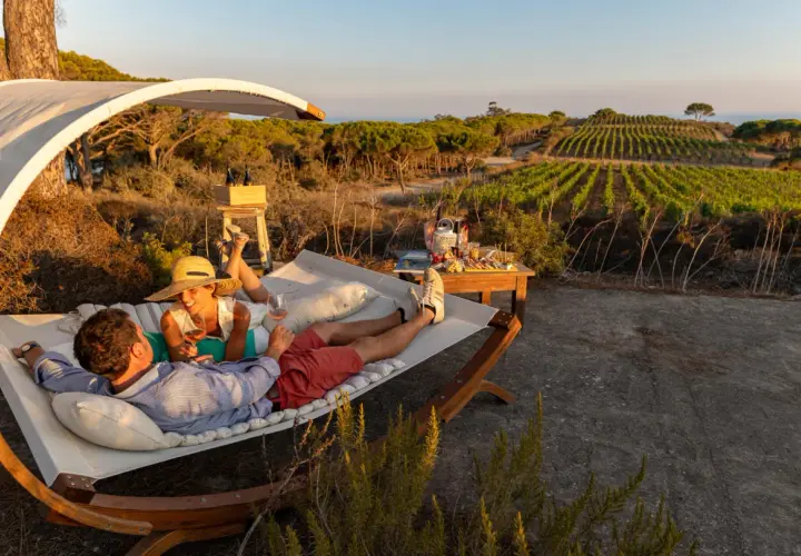 Coppia rilassata su un'amaca con vista su vigneti e mare, sorseggiando vino. Un perfetto sorgeto Ischia aperitivo al tramonto.
