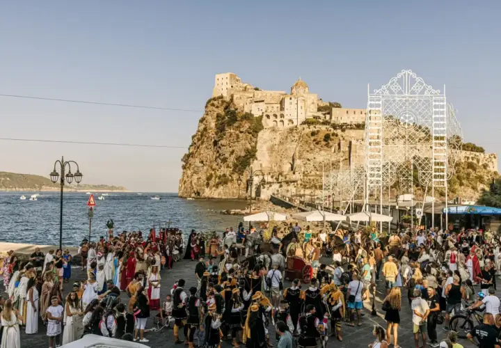 Festa in costume sul lungomare, con il castello sullo sfondo. La spiaggia degli inglesi è animata da figuranti e spettatori.