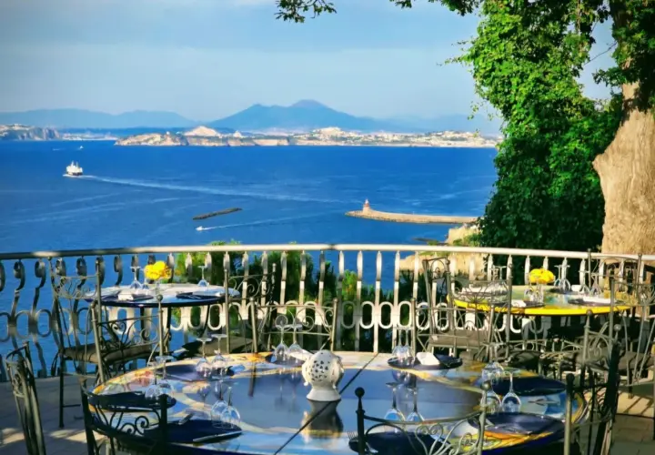 Tavoli apparecchiati con vista mare, un invito a cenare in uno dei ristoranti di Casamicciola. Il Vesuvio sullo sfondo.