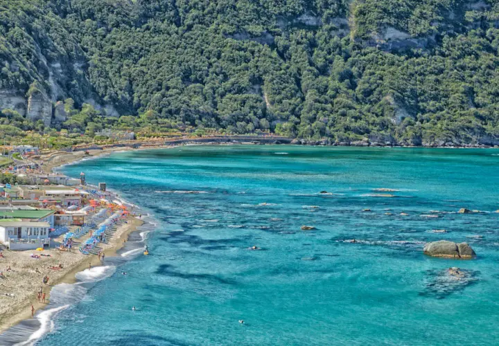 La spiaggia di Citara, con le sue acque cristalline e la rigogliosa vegetazione alle spalle, accoglie bagnanti e ombrelloni colorati.