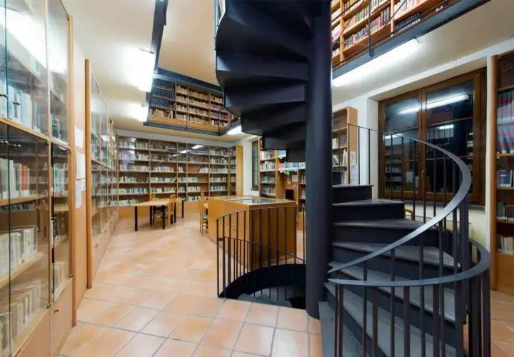 Interno della biblioteca antoniana ischia con scaffali pieni di libri, tavoli e una scala a chiocciola nera.