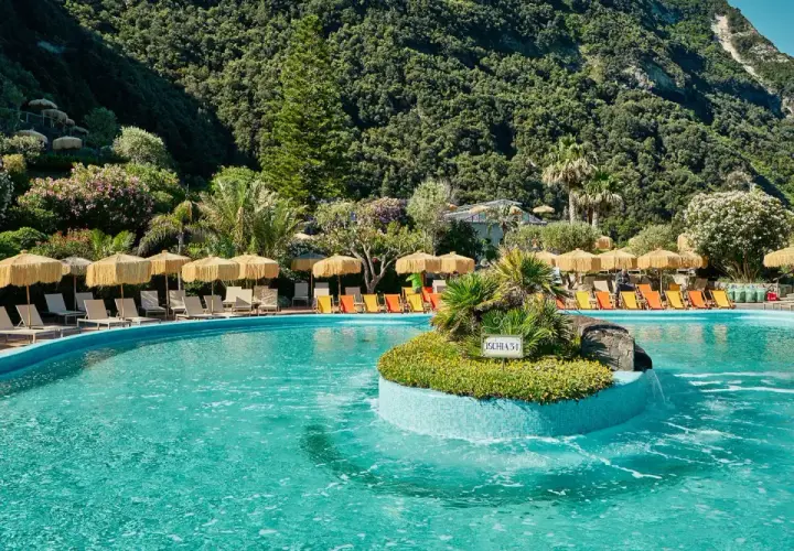 Piscina con lettini e ombrelloni a Ischia, immersa nel verde rigoglioso. Un'oasi di relax che ricorda la forza del **Tifeo** che dorme sotto l'isola.