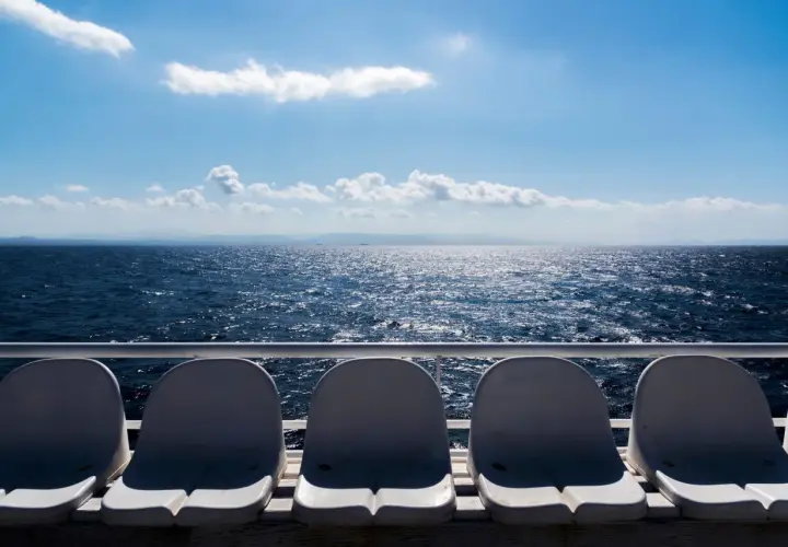 Sedili vuoti su un traghetto, con il mare blu scintillante e le montagne all'orizzonte. La differenza tra aliscafo e traghetto è evidente nella velocità e nel comfort.