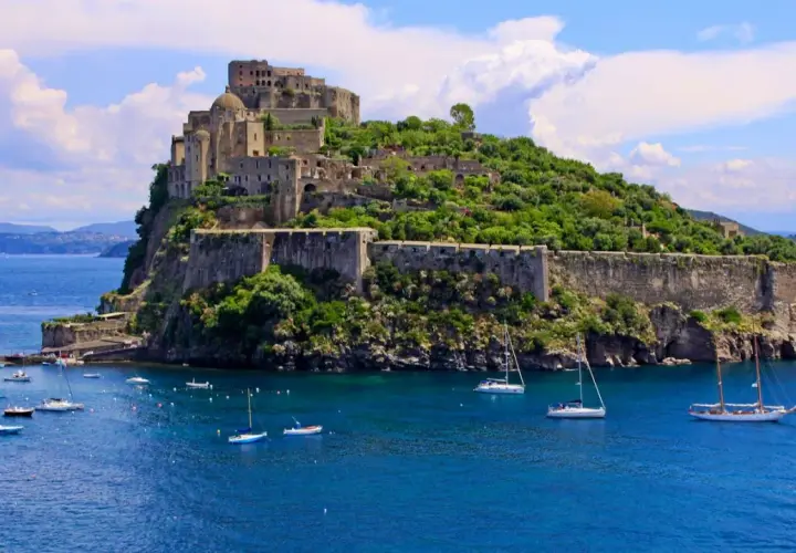 Ischia Ponte, con il maestoso Castello Aragonese che domina l'isola verdeggiante, circondato da un mare blu intenso e barche a vela.