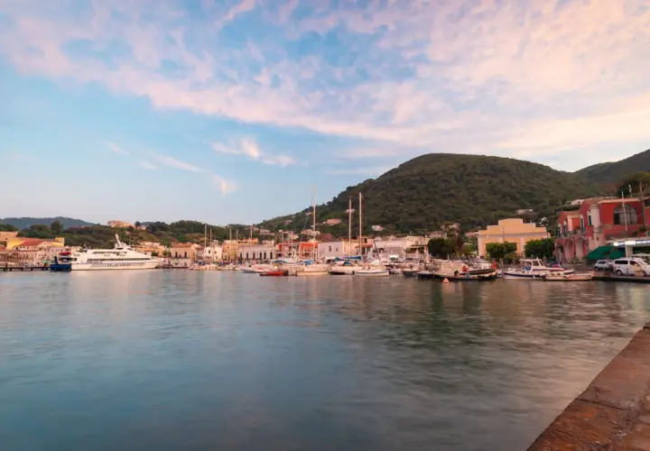 I **porti di Ischia** al tramonto, con barche ormeggiate e colline verdi sullo sfondo.