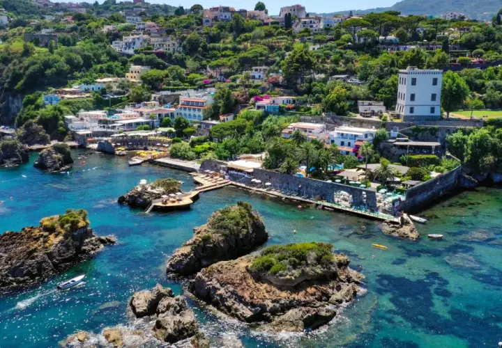 Baia di Cartaromana con rocce e acque cristalline. Case arroccate sulla collina. Scopri come arrivare a questa incantevole spiaggia.