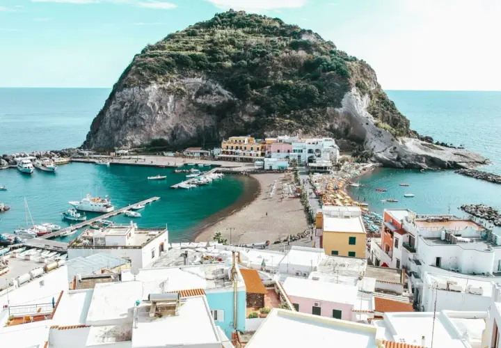 Baia con barche e case colorate a Ischia, con la rocca verde che domina il mare. Le cantine di Ischia offrono un panorama mozzafiato.