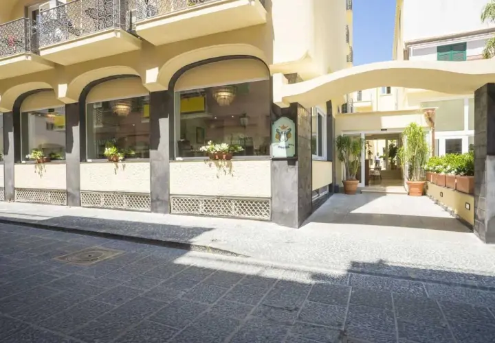 Ingresso elegante del **hotel Bristol Ischia**, con ampie vetrate, piante verdi e un'insegna storica.
