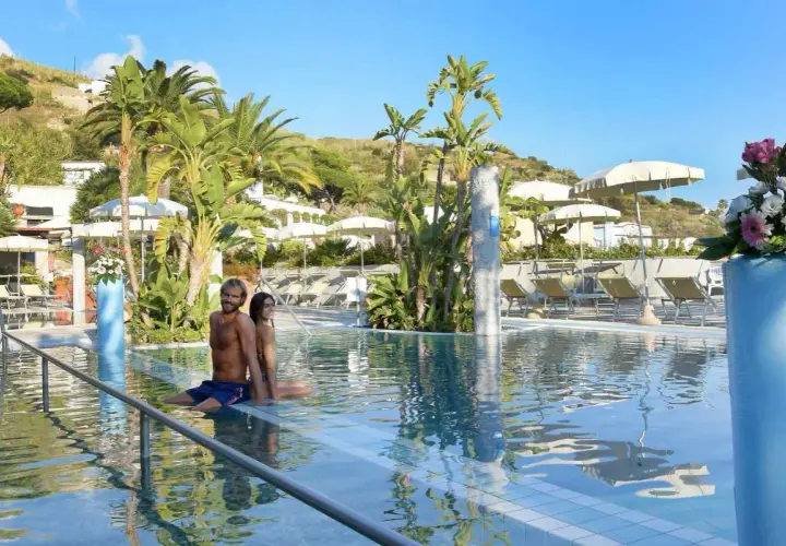 Coppia rilassata in piscina, circondata da palme e lettini, in un resort alle terme Ischia.