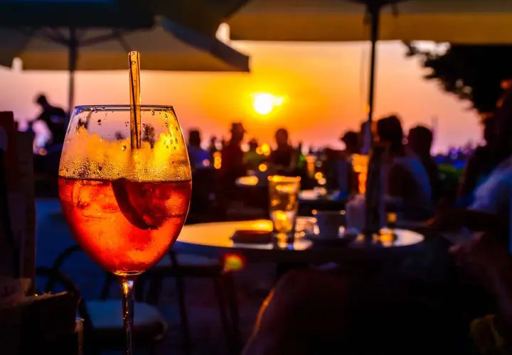 Un aperitivo rinfrescante con vista sul tramonto a Ischia centro sera. Persone sedute ai tavoli, ombrelloni e il sole che cala all'orizzonte.