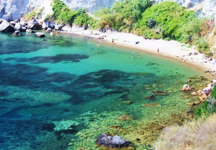 Acque cristalline e sabbia dorata nella spiaggia delle monache, incastonata tra scogliere rocciose e vegetazione rigogliosa.