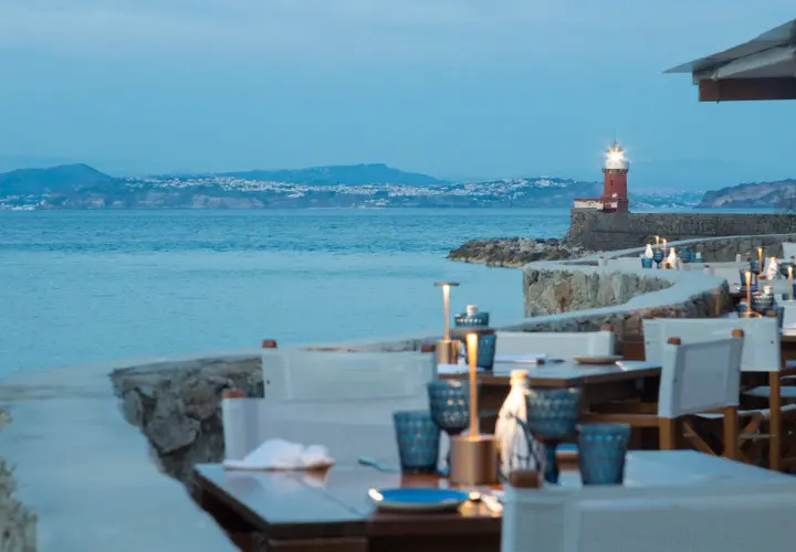 Tavoli apparecchiati con vista sul mare e un faro rosso, un invito a cena a Ischia.