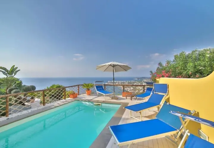 Piscina con lettini blu e vista mare a Ischia. Un angolo di paradiso, un dolce Poseidon che invita al relax.