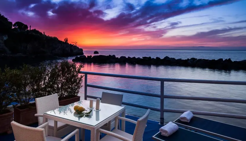 Terrazza con tavolo e sedie, lettini prendisole e un tramonto mozzafiato sul mare, un sogno in un blu resort Ischia.