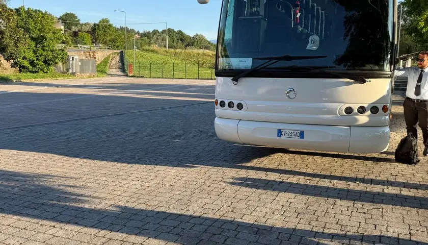 Un bus bianco attende su un parcheggio lastricato, pronto a percorrere le strade di Ischia. Un autista in divisa controlla il bagaglio.