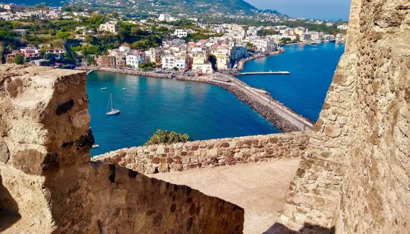 Vista panoramica del porto di Ischia, con i traghetti in attesa e le case colorate che si affacciano sul mare blu.