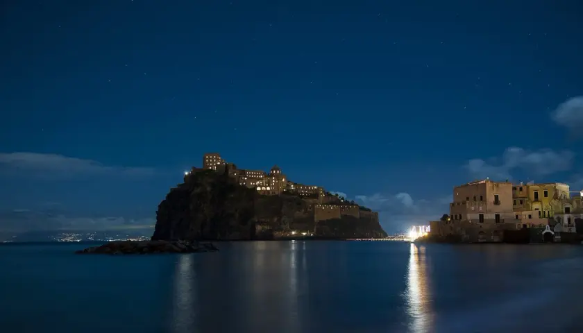 Castello Aragonese illuminato di notte, riflesso sull'acqua, sotto un cielo stellato. Un'opera di Gabriele Mattera.