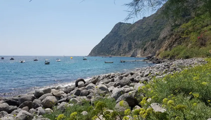 La baia della Scarrupata, con le sue rocce levigate e il mare azzurro, accoglie piccole imbarcazioni. Un pontile si protende nell'acqua.