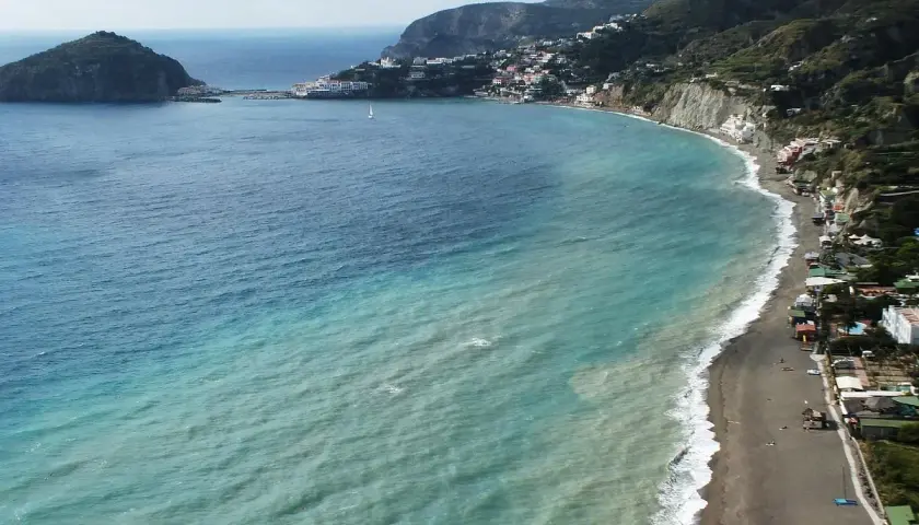 Vista aerea della spiaggia dei pescatori a Ischia, con case colorate aggrappate alla costa e un mare turchese.