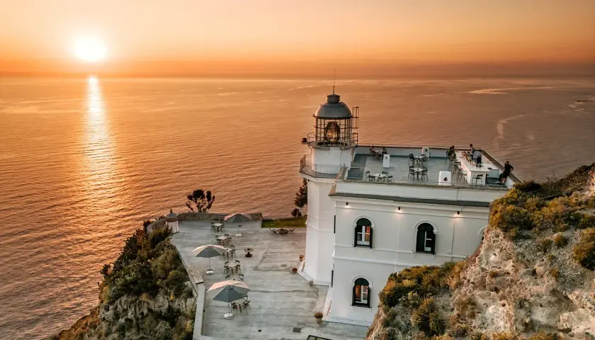 Hotel Faro Punta Imperatore a Ischia, con il sole che tramonta sul mare. Tavolini all'aperto e un bar sul tetto.