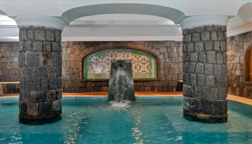 Piscina interna con fontana a cascata, colonne in pietra e piastrelle decorative. Un angolo di relax alle terme di Lacco Ameno.
