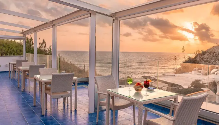 Terrazza con vista mare al tramonto, ideale per chi cerca dove alloggiare a Ischia senza macchina. Tavoli apparecchiati per aperitivo.