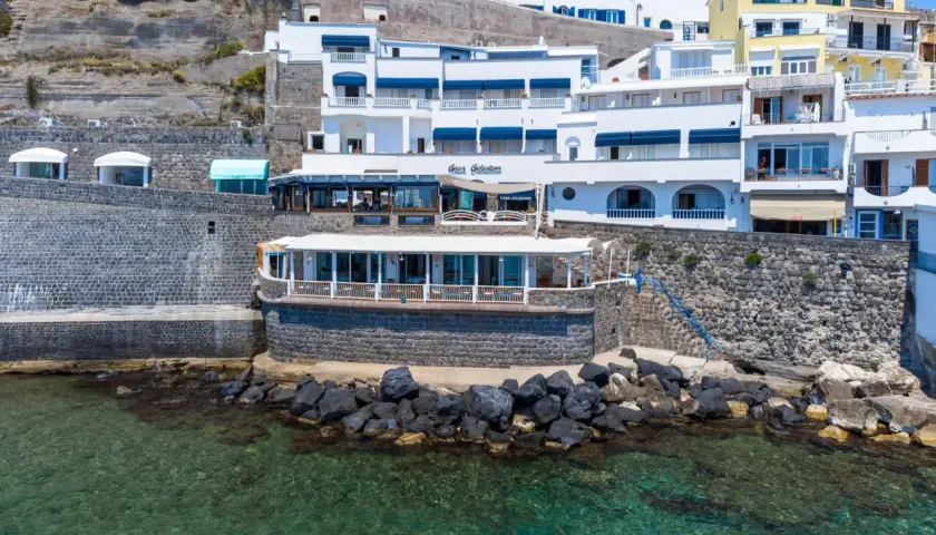 Hotel Celestino Ischia, con la sua architettura bianca e blu, si affaccia sul mare cristallino, incastonato nella roccia.